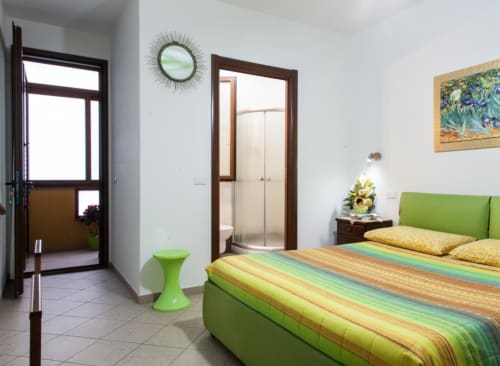 Chambre lumineuse avec lit vert citron, linge de lit rayé coloré, mobilier en bois et vue sur le jardin à l'hôtel Al Mare à Torre