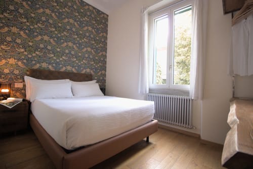 Luminosa piccola camera doppia a Porta Tosa B&B Milano con carta da parati decorativa, biancheria bianca, finestre con vista giardino e arredamento in legno