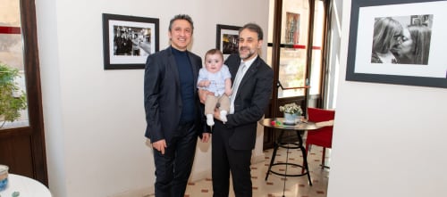 Due uomini in abito con una bambina piccola all'hotel Stella CasaBono a Sulmona, fotografie incorniciate sulle pareti dietro di loro