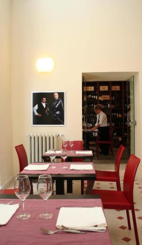 Elegant dining room at Stella CasaBono hotel in Sulmona with burgundy tables, red chairs, and portrait artwork