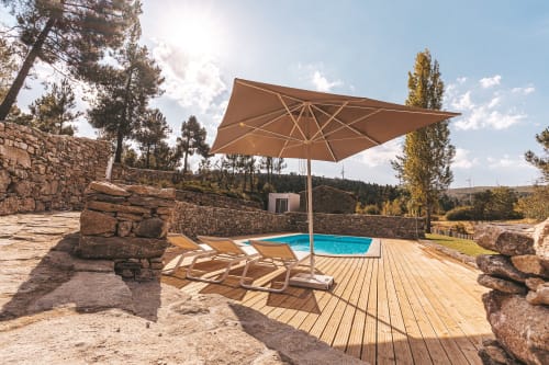 Piscina exterior nos Moinhos d’Antoninha, Serra de Leomil, Moimenta da Beira, com espreguiçadeiras e guardan-sol, integrada num espaço de pedra e madeira, rodeado pela paisagem serena da região.