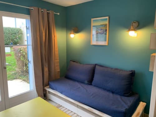 Chambre cosy du gîte Locations Loc'Maria, Belle Île avec murs bleu canard, lit de jour bleu, rideaux marron et accès à la vue sur jardin