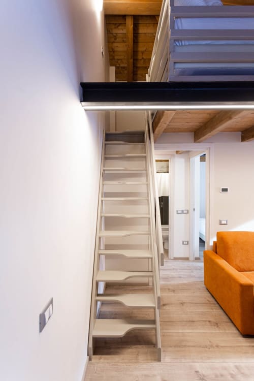 Scala moderna del loft a Villa Brioschi ad Aprica con gradini bianchi, travi in legno e sedute arancioni