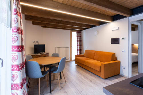 Moderno appartamento a Villa Brioschi ad Aprica con divano arancione, tavolo da pranzo, TV, travi in legno e accesso al balcone