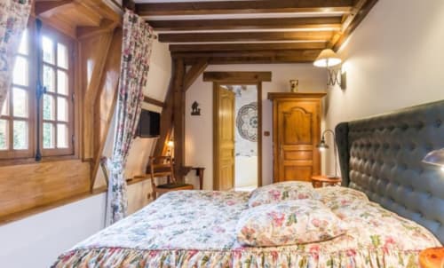 Chambre rustique du Moulin d'Ajon avec parure florale, poutres apparentes et vue sur le jardin
