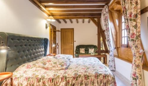 Chambre de charme au Moulin d'Ajon avec poutres apparentes, tête de lit capitonnée et literie fleurie donnant sur les jardins