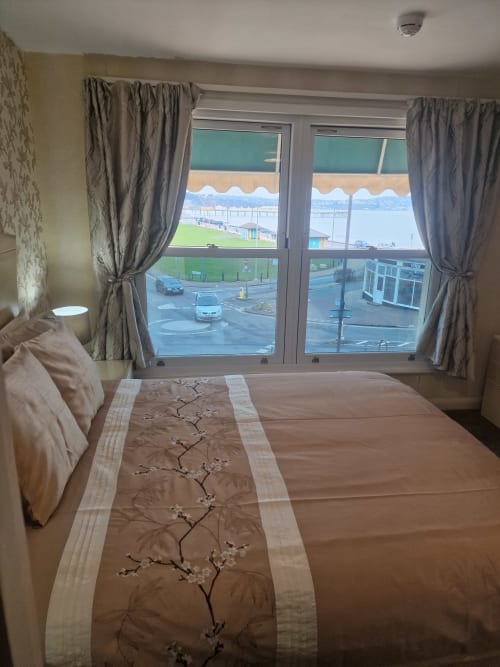 Double bedroom at The Sands Hotel in Paignton with sea view through large windows, brown bedding, and grey curtains
