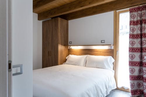 Camera moderna presso la Residence Villa Brioschi ad Aprica con travi in legno, letto incorporato, biancheria bianca e motivi rossi