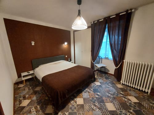 Chambre moderne au Gîte Le Comtois en Saône avec mur d'accent marron, luminaire suspendu et sol à motifs.