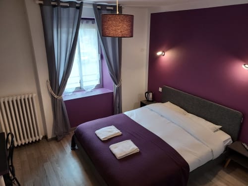 Chambre moderne à la Maison d'hôtes Le Comtois en Saône avec mur d'accent violet, lit queen et lumière naturelle