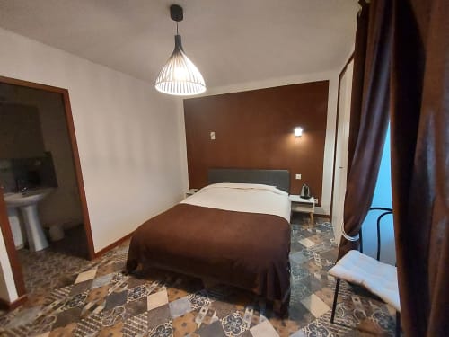 Chambre aux tons marron du gîte Le Comtois à Saône avec luminaire suspendu, lit sombre et vue sur la ville