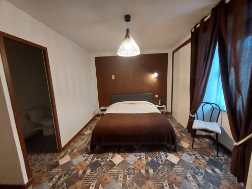 Chambre moderne au gîte Le Comtois à Saône avec mur d'accent marron, literie blanche, luminaire suspendu et vue sur la ville
