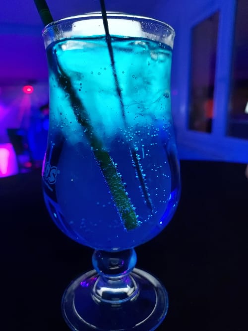 Élégant cocktail bleu éclatant garni de glaçons et paille au Comtois, Saône. Verre raffiné illuminé par l'ambiance nocturne.