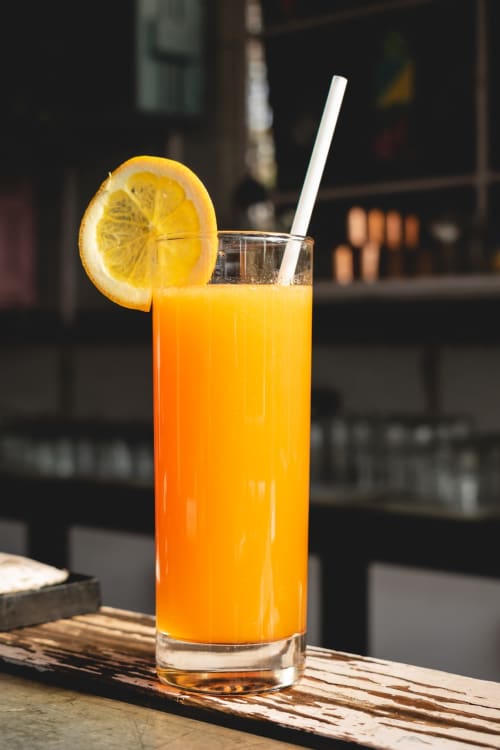 Cocktail à base de jus d'orange frais, tranche de citron et paille au Comtois, charmant gîte en Saône, France.