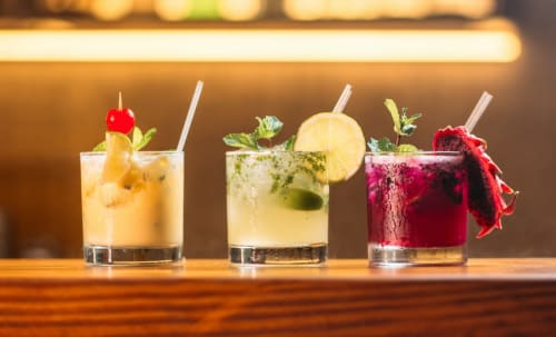 Trois cocktails colorés avec garnitures fraîches au comptoir du bar du Comtois, gîte en Saône, France.