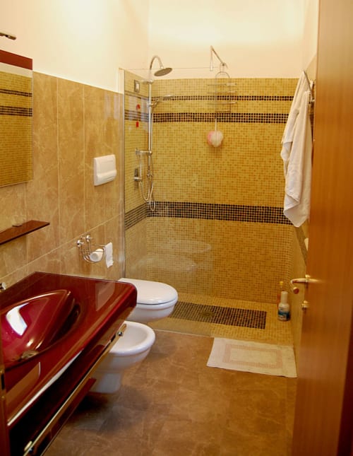 Modernes Badezimmer im Hotel Stella CasaBono in Sulmona mit golden gefliester Dusche, rotem Waschtisch und eleganten Armaturen
