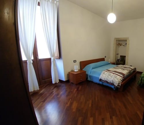 Geräumiges Schlafzimmer im Hotel Stella CasaBono in Sulmona mit Holzbett, blauer Bettwäsche und Fenster mit weißen Vorhängen