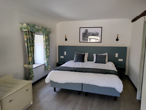 Modern bedroom at Le Moulin Des Ramiers with king bed, green headboard, garden view window, and contemporary decor in Crupet.