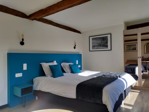 Modern bedroom with blue headboard, king bed, exposed beams, and garden view at Le Moulin Des Ramiers hotel in Crupet