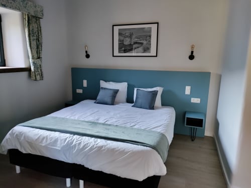 Modern hotel bedroom at Le Moulin Des Ramiers with teal headboard, white bedding, and twin blue pillows