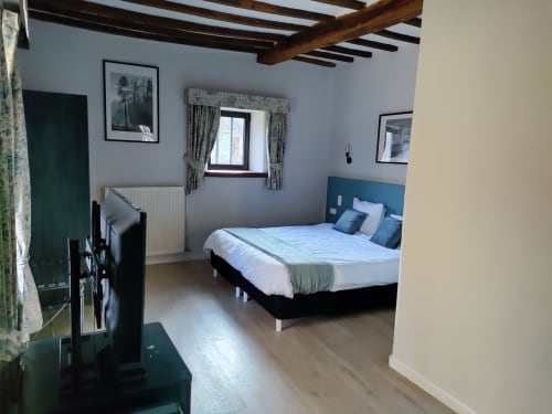Modern double bedroom at Le Moulin Des Ramiers with king bed, blue headboard, wooden beams, and garden view window