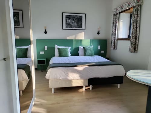 Modern hotel room at Le Moulin Des Ramiers with green headboard, king bed, white bedding, wooden floor, and garden views