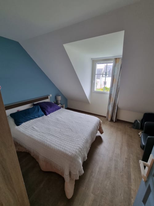Chambre moderne dans un appartement de Belle Île en Mer avec un mur d'accent bleu-vert, lit queen-size, plafond mansardé, fenêtre vue jardin et bois