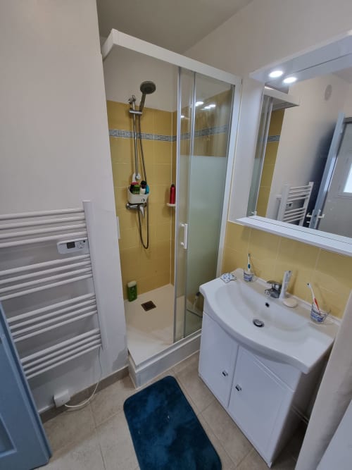 Salle de bain moderne avec carrelage jaune, douche vitrée, lavabo blanc et sèche-serviettes chauffant de l'appartement Locmaria