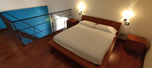Modernes Hotelzimmer in der Stella CasaBono in Sulmona mit Holzboden, Queensize-Bett, Nachttischleuchten und blauem Geländer.