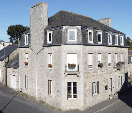 Les Forges Du Lou, une maison d'hôtes en pierre à Jugon-les-Lacs, avec toits mansardés, fenêtres aux cadres blancs et charme d'époque.