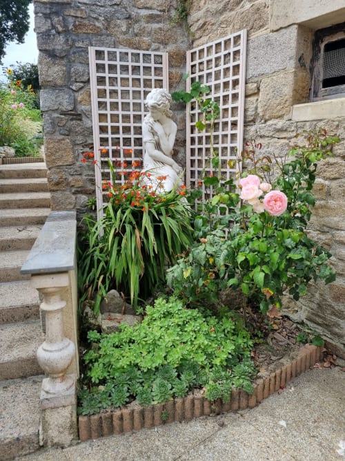 Cour fleurie des Forges Du Lou avec statue, treillages blancs et plantes fleuries à Jugon-les-Lacs