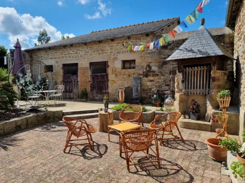 Cour en pierre rustique des Forges Du Lou avec mobilier en osier et drapeaux de prière colorés