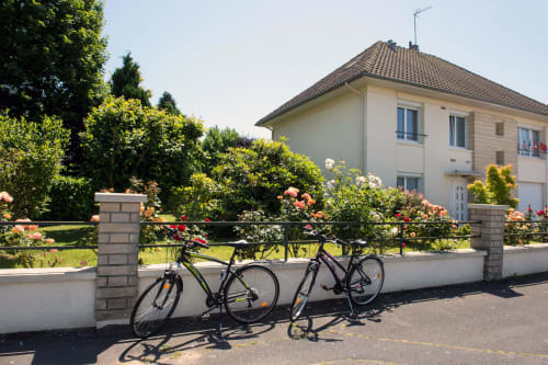 Two bicycles leaning against fence of Au Gite d'Isigny B&B in Isigny-sur-Mer with flowering gardens and countryside home