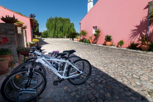 Bicicletas estacionadas no pátio da Casa das Jardas, uma casa rural em Ladoeiro com paredes cor-de-rosa e vasos de terracota.
