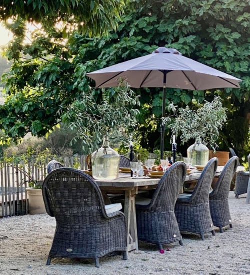 Outdoor dining area at Saint Martin B&B in Ollioules with wicker chairs, umbrella, and lush garden backdrop.