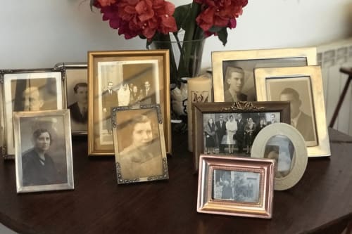 Fotografias familiares vintage e retratos emoldurados exibidos em mesa de madeira escura com flores vermelhas na Casa das Jardas rural