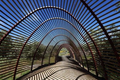 Curved metal arbor tunnel with striped shadows at Casa das Jardas rural lodge in Ladoeiro, Portugal