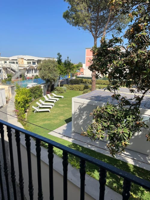 Cortile dell'appartamento Palazzo Porta a Procida con sdraio, prato verde e alberi mediterranei sotto cielo sereno