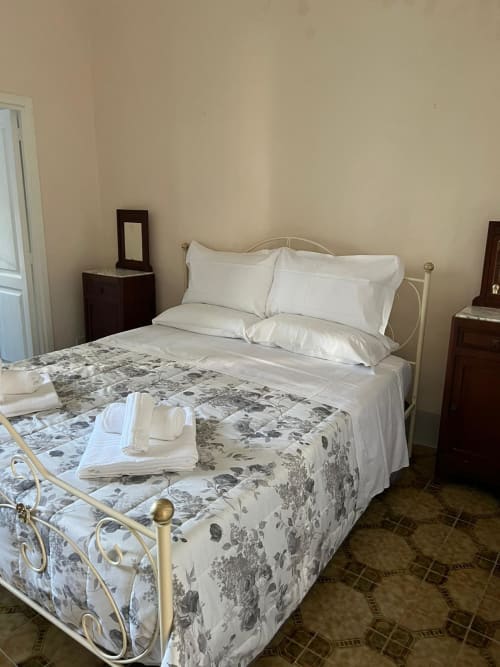 Camera luminosa del Palazzo Porta B&B a Procida con letto in ferro bianco, biancheria floreale e pareti color crema