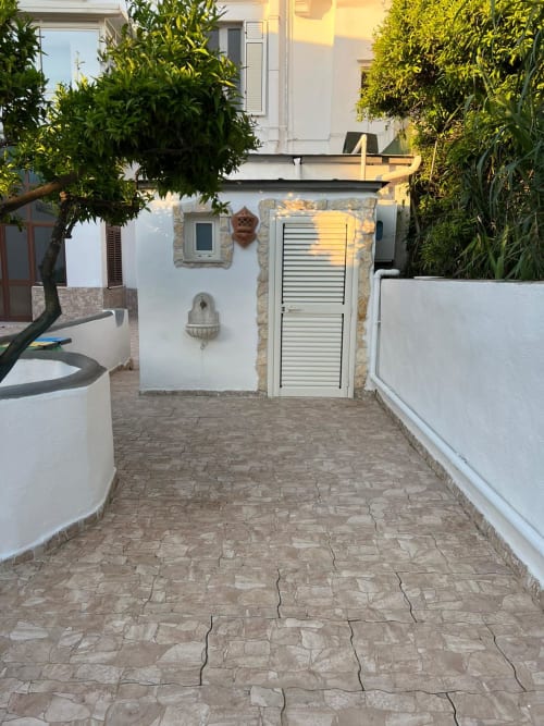 Ingresso del giardino di Palazzo Porta a Procida con cortile in terracotta, muri bianchi e rigogliosa vegetazione