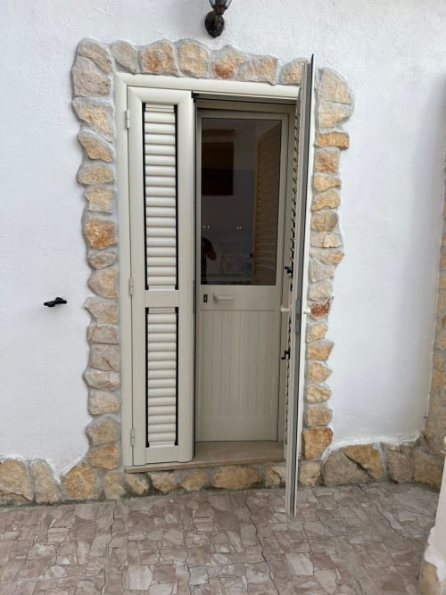 Porta color crema con pannelli a persiana aperta al Palazzo Porta di Procida, ingresso interno verso appartamento con vista giardino.