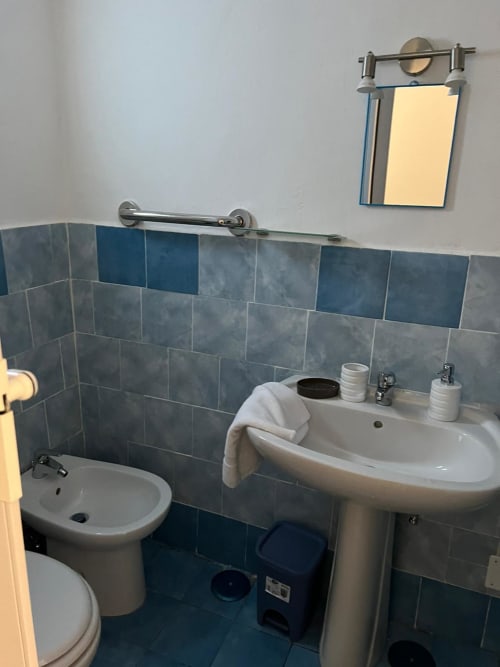 Bagno presso il Palazzo Porta BnB a Procida con pareti piastrellate, toilette, lavabo a piedistallo e specchio
