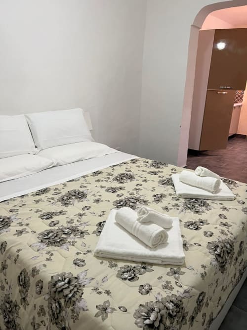 Accogliente letto con biancheria a fiori e asciugamani bianchi nell'appartamento Palazzo Porta a Procida