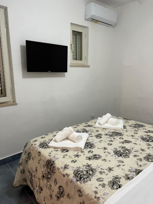 Camera moderna al Palazzo Porta BnB a Procida con TV a parete, aria condizionata e biancheria floreale con asciugamani arrotolati