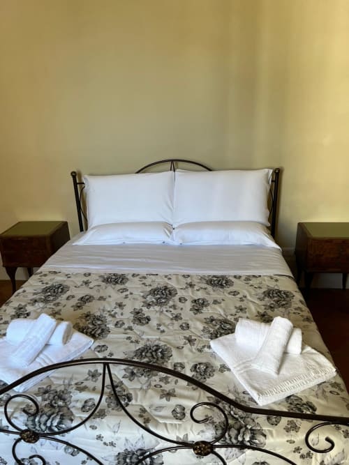 Camera accogliente al Palazzo Porta B&B di Procida con letto in ferro, cuscini bianchi, copriletto con motivi floreali e legno scuro