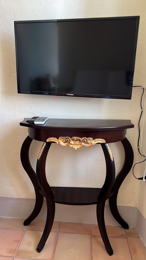 Televisore Hyundai montato sopra una consolle in legno scuro ornamentale con telecomando a Palazzo Porta, Procida