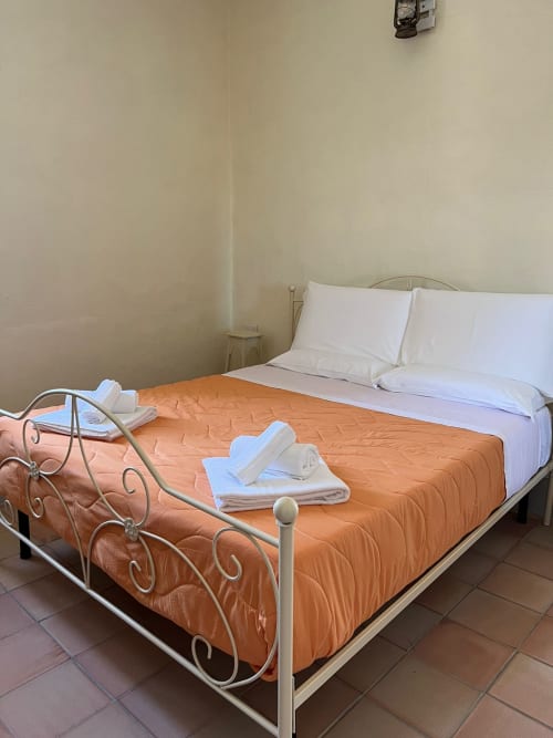 Camera da letto a Palazzo Porta, Procida con letti gemelli, coperta arancione e cuscini bianchi