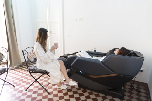 Donna in veste bianca che utilizza una poltrona massaggiante nella camera dell'hotel B&B I MORI Catania con vista sulla città