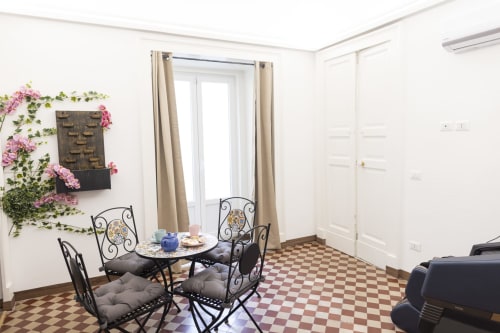 Camera luminosa al B&B I MORI Catania con sedie in ferro battuto, fiori rosa e pavimento piastrellato a scacchi