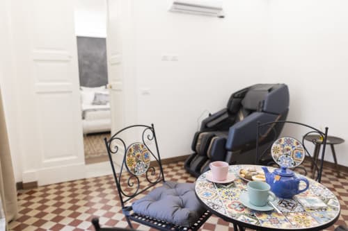 Sala Sovereign Herb del B&B I MORI Catania con tavolo decorativo, poltrona massaggio e area relax con vista sulla città.